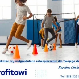 Dzieci ćwiczą grę w piłkę nożną na sali gimnastycznej, slalom między pomarańczowymi pachołkami, widoczny fragment logo firmy ubezpieczeniowej.