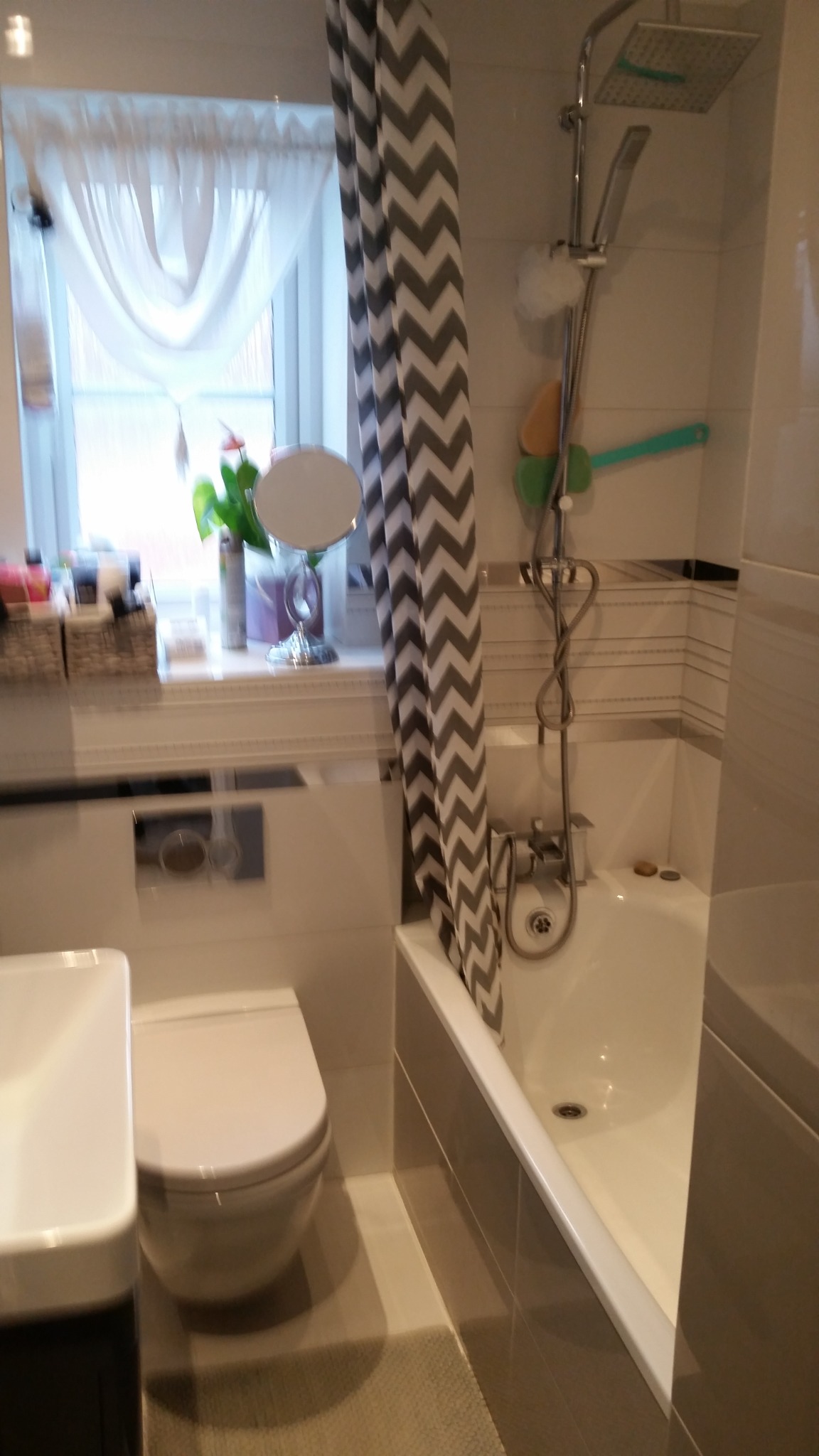 Ukończona łazienka z wanną, prysznicem, toaletą podwieszaną i zasłoną w zygzaki, widok z bliska na armaturę i akcesoria.