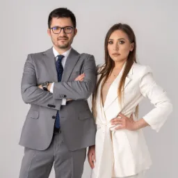 Portret dwojga prawników: mężczyzna w szarym garniturze z zegarkiem i kobieta w białym komplecie, oboje patrzą w obiektyw na jasnym tle.