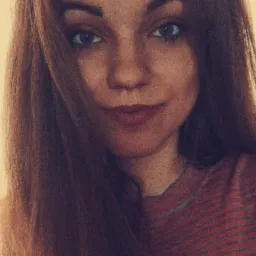 Portret młodej kobiety z długimi, rudymi włosami i niebieskimi oczami, ubrana w bluzkę w paski.