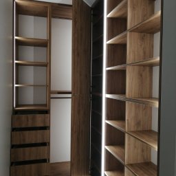 byMGdesigns - Wnętrze szafy wnękowej z otwartymi drzwiami, oświetleniem LED wzdłuż krawędzi półek i szuflad, wykończonej w okleinie drewnopodobnej z widocznymi usłojeniami.