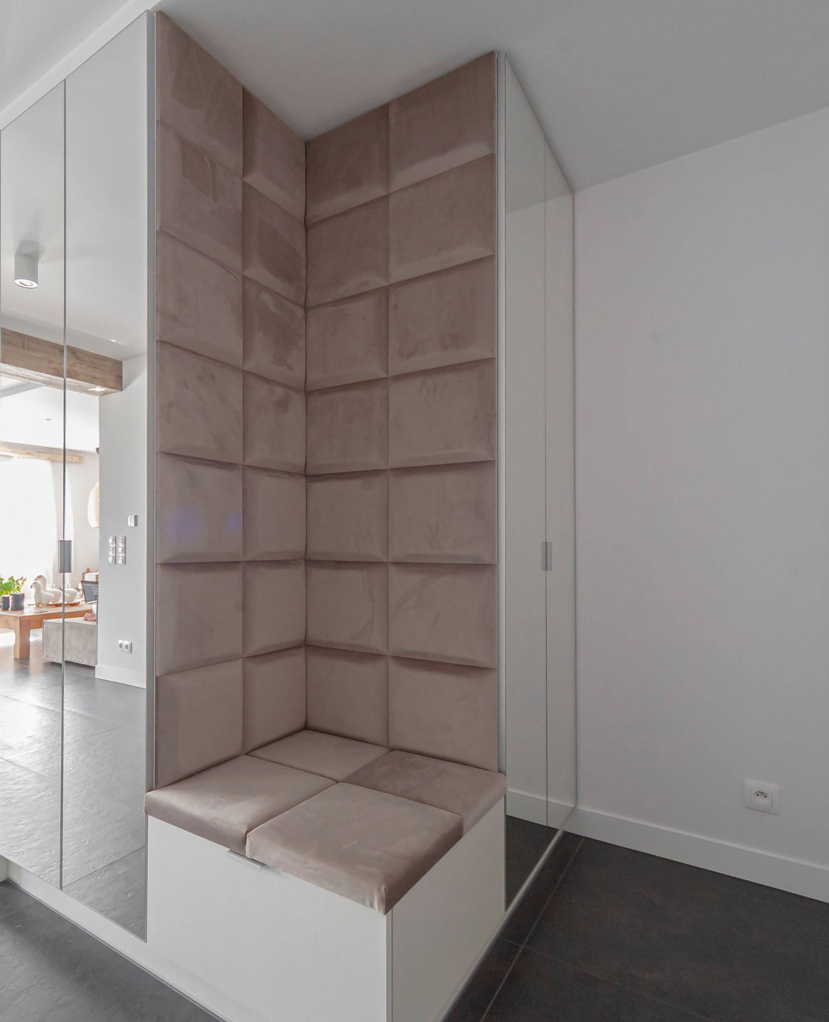 Wnęka wejściowa z siedziskiem obitym beżowym, pikowanym materiałem, otoczona lustrami, widok na salon w tle.