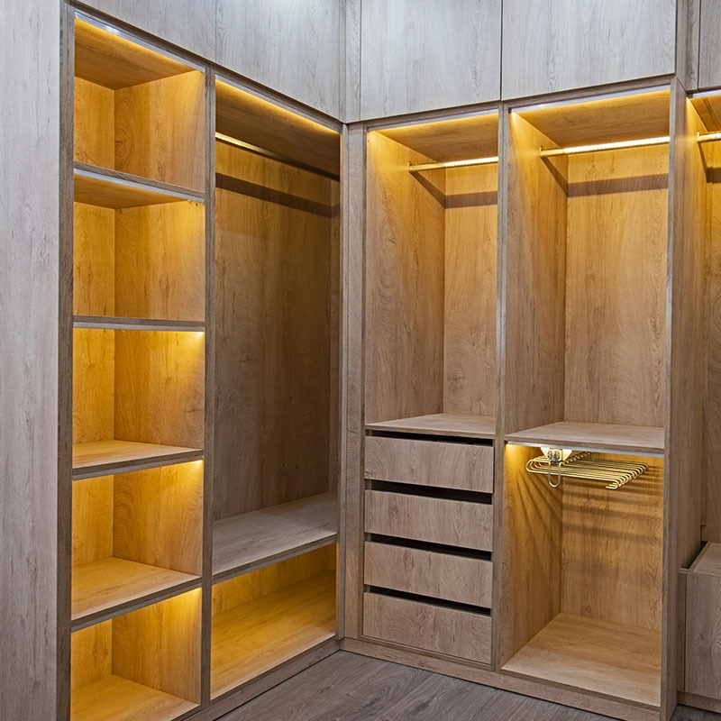 Wnętrze garderoby narożnej z oświetleniem LED, drewnopodobne wykończenie, szuflady i półki.