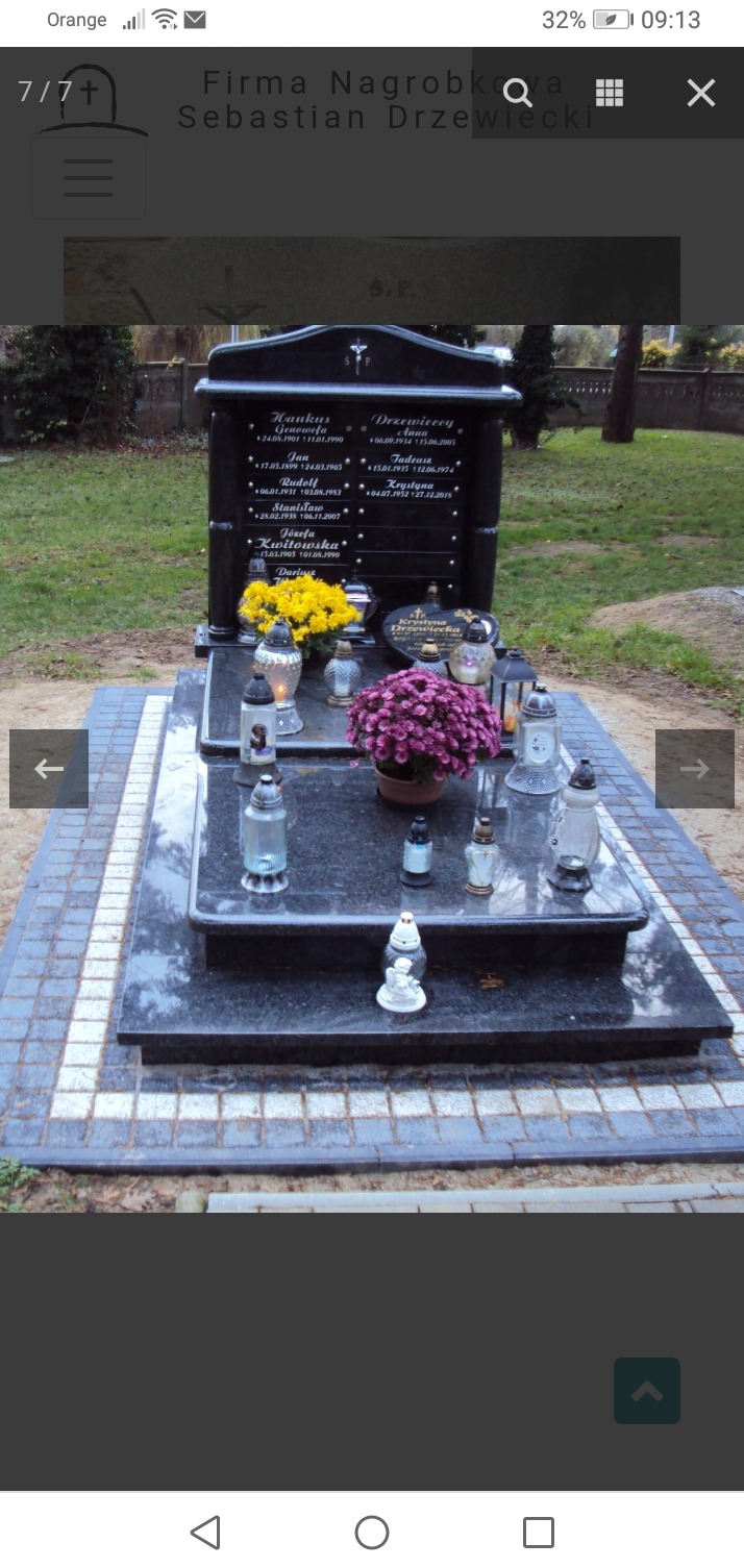 Czarny, polerowany nagrobek z wygrawerowanymi imionami i datami, ozdobiony żółtymi i fioletowymi kwiatami w doniczkach oraz zapalonymi zniczami, otoczony kostką brukową.