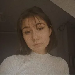 Portret młodej kobiety z grzywką i delikatnym makijażem oczu, ubrana w białą bluzkę z golfem, w stonowanej kolorystyce.