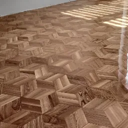 Ukończona podłoga z parkietu ułożonego w geometryczny wzór kostki, z widocznymi promieniami słońca wpadającymi przez okno.