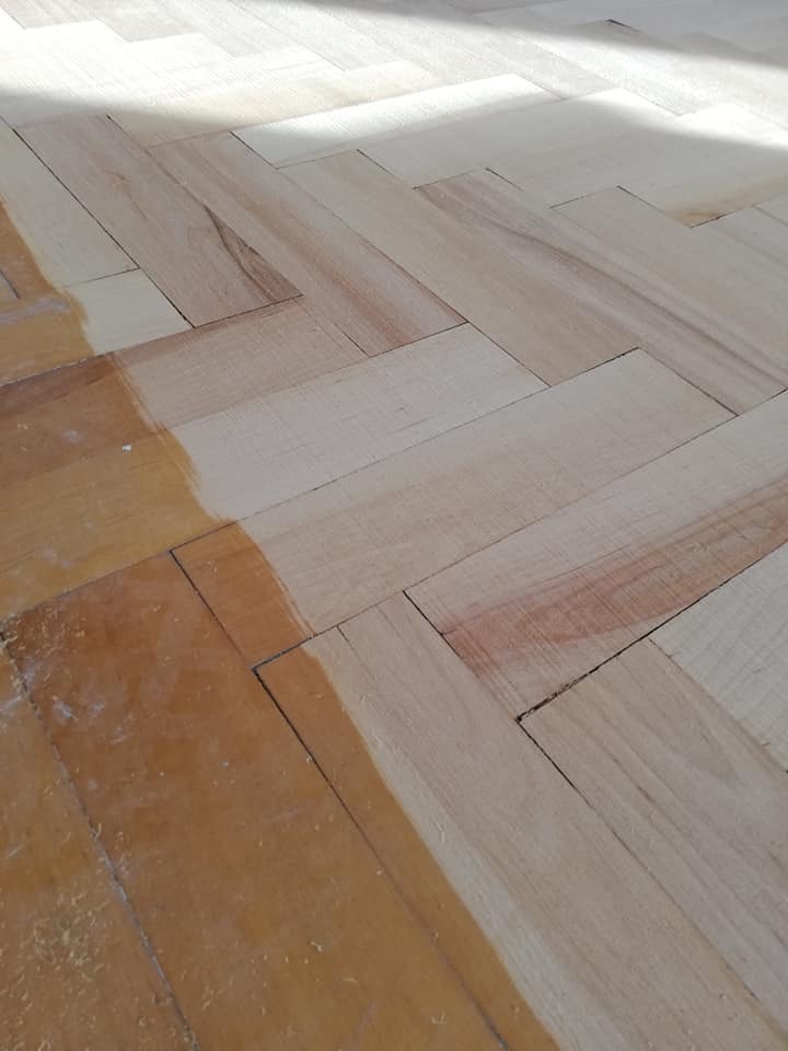 Parkiet ułożony w jodełkę, częściowo po renowacji, z widoczną różnicą w kolorze i strukturze drewna w oświetleniu słonecznym.