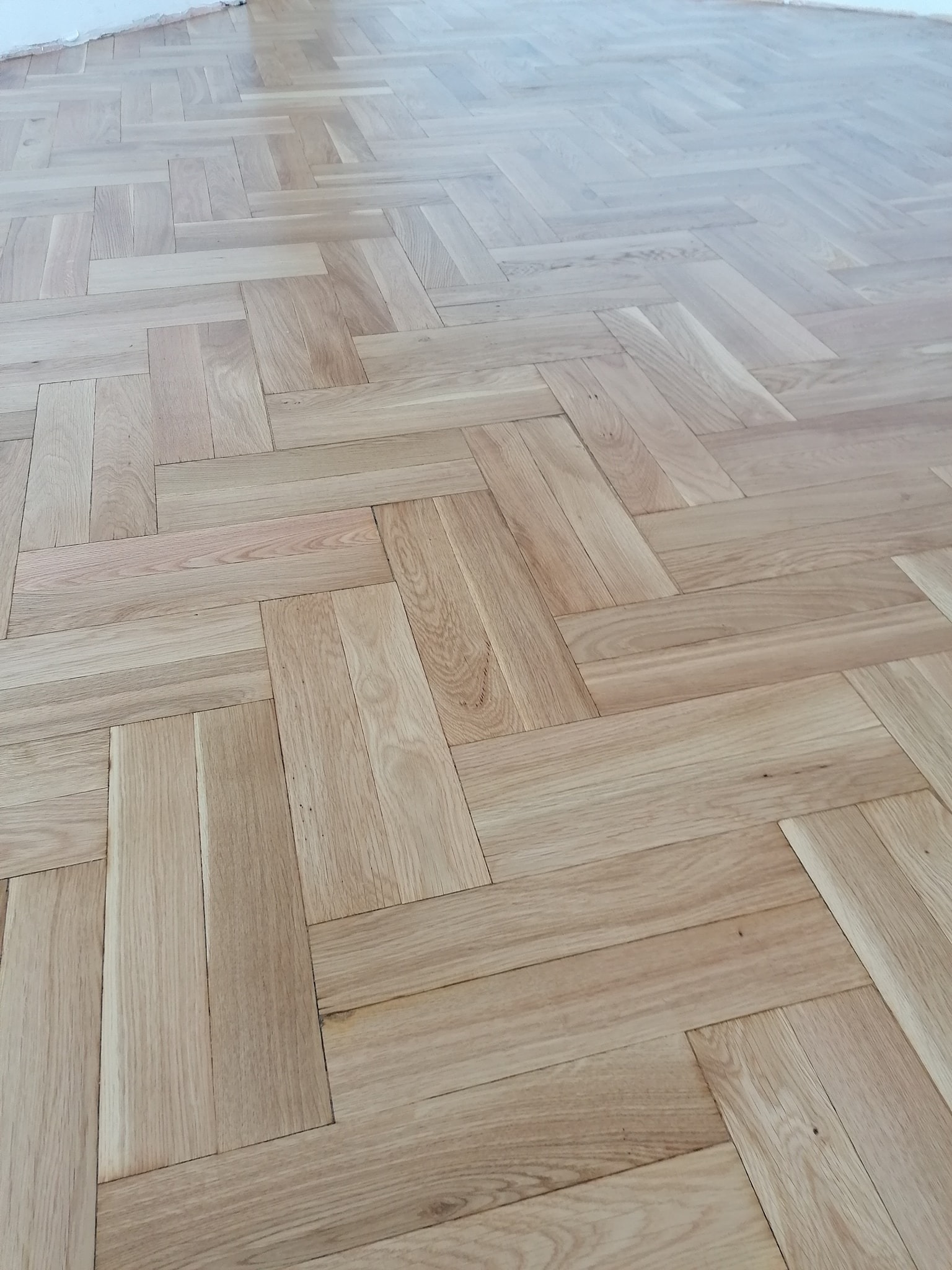 Ułożona parkietowa podłoga w jodełkę francuską, jasne drewno, widok z góry, świeżo po lakierowaniu.