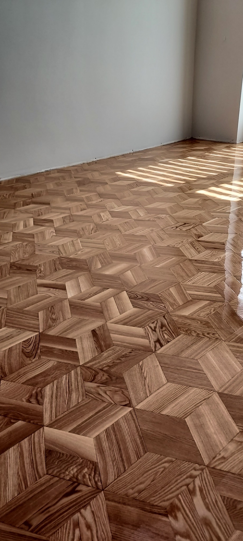 Ukończona podłoga z parkietu ułożonego w geometryczny wzór kostki, z widocznymi promieniami słońca wpadającymi przez okno.