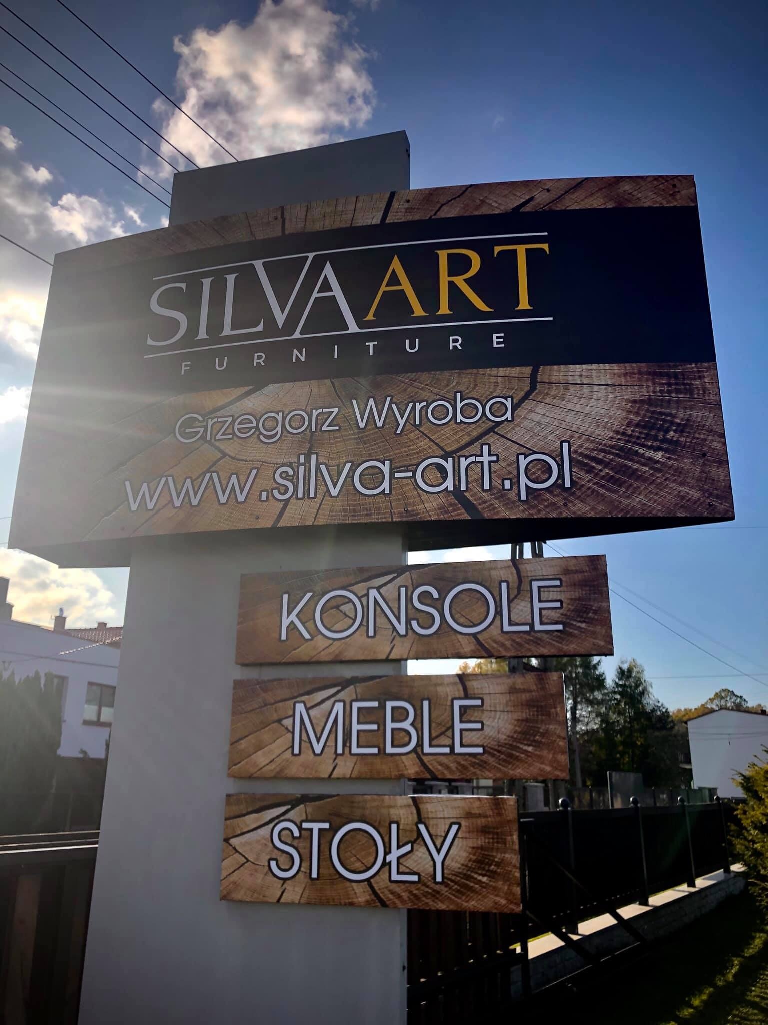 Tablica reklamowa firmy meblarskiej Silva Art z nazwą, danymi kontaktowymi i ofertą: konsole, meble, stoły. Tło imitujące przekrój drewna.