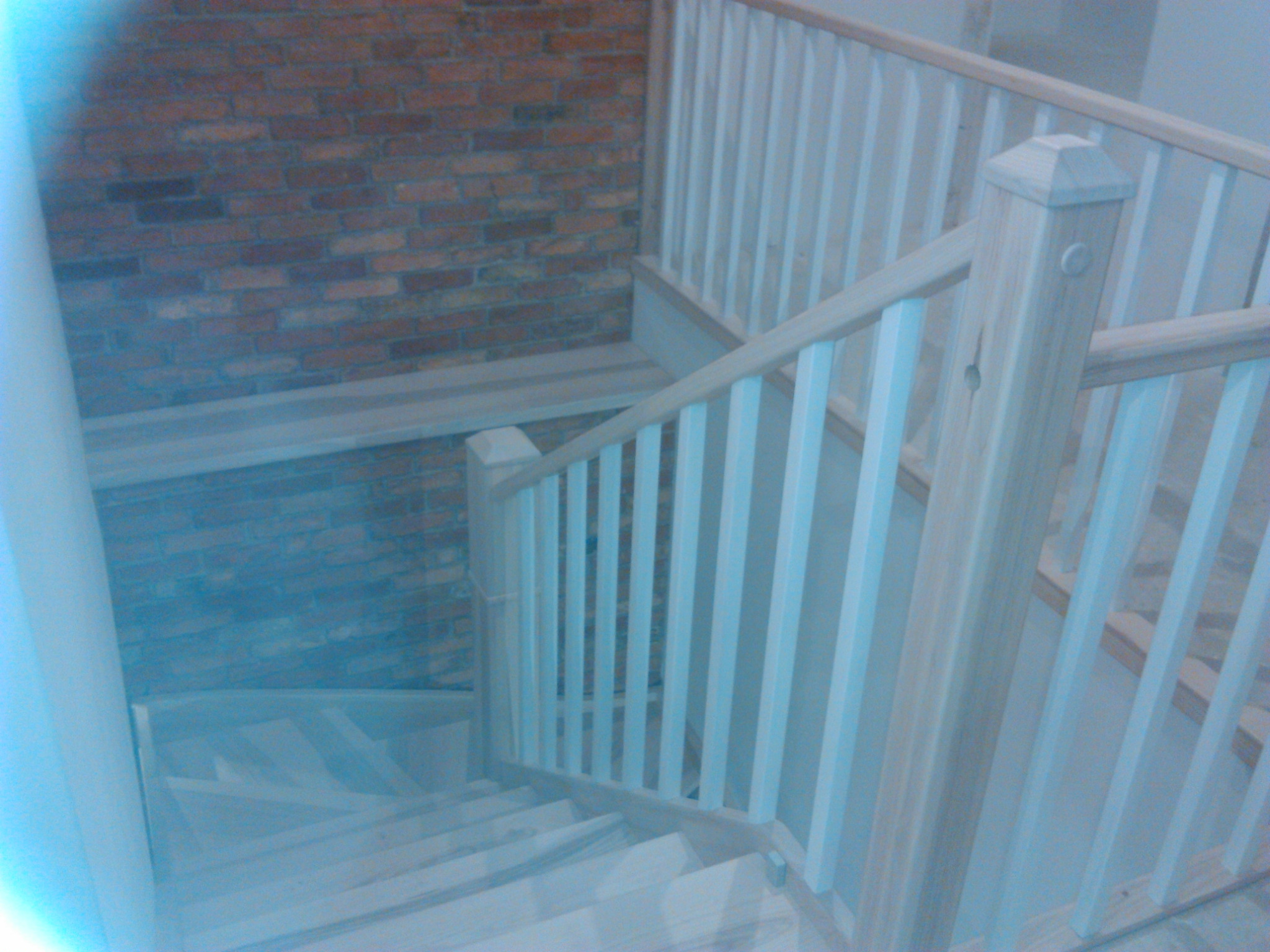 Drewniane schody z jasnymi, pomalowanymi na biało balustradami, widok z góry, ceglana ściana w tle.