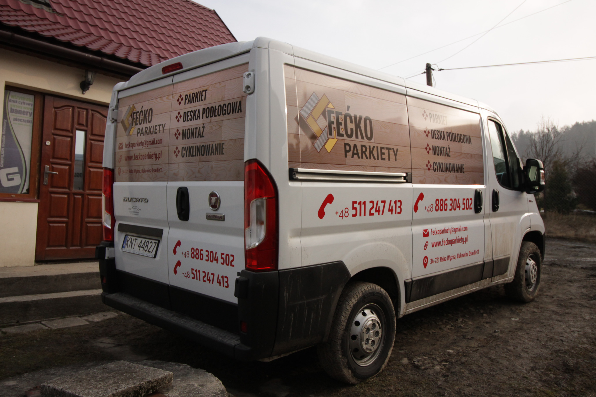 Oklejony biały samochód dostawczy Fiat Ducato firmy Fecko Parkiety z reklamą usług parkieciarskich: parkiet, deska podłogowa, montaż, cyklinowanie, zaparkowany przed budynkiem z czerwonym dachem.