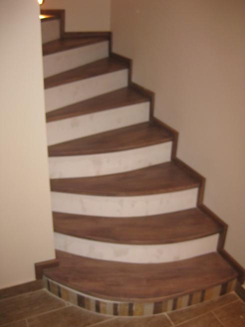 Spiralne schody z drewnianymi stopniami o zaokrąglonym kształcie, wykończone płytkami mozaikowymi u podstawy, z białymi podstopnicami.