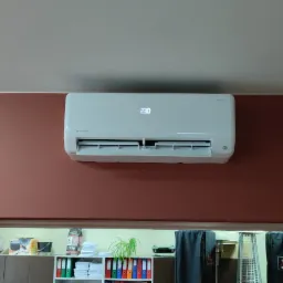 Biały klimatyzator na ścianie w kolorze terakoty, z wyświetlaczem wskazującym temperaturę 23 stopnie Celsjusza, widok z dołu.