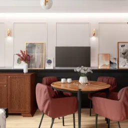 Jadalnia w ciepłej tonacji z drewnianym stołem, czterema bordowymi krzesłami, komodą i przeszkloną witryną, dekorowana kwiatami, grafikami i złotymi akcentami oświetleniowymi.