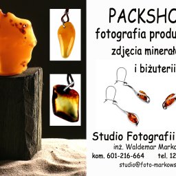 FOTO Markowski - Fotografia produktowa: Bursztyn bałtycki na drewnianym postumencie, wisior z bursztynem, srebrne kolczyki i naszyjnik z bursztynem na jasnym tle z danymi kontaktowymi studia fotograficznego.