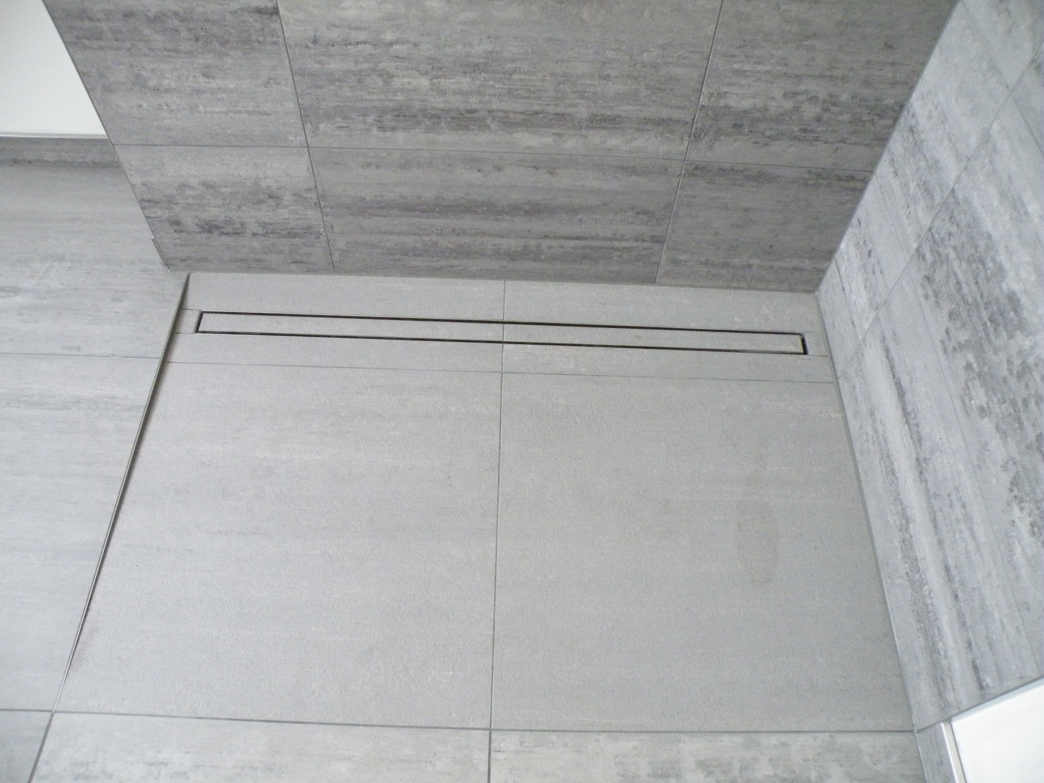 Nowoczesna łazienka z szarymi płytkami imitującymi beton i liniowym odpływem podłogowym.