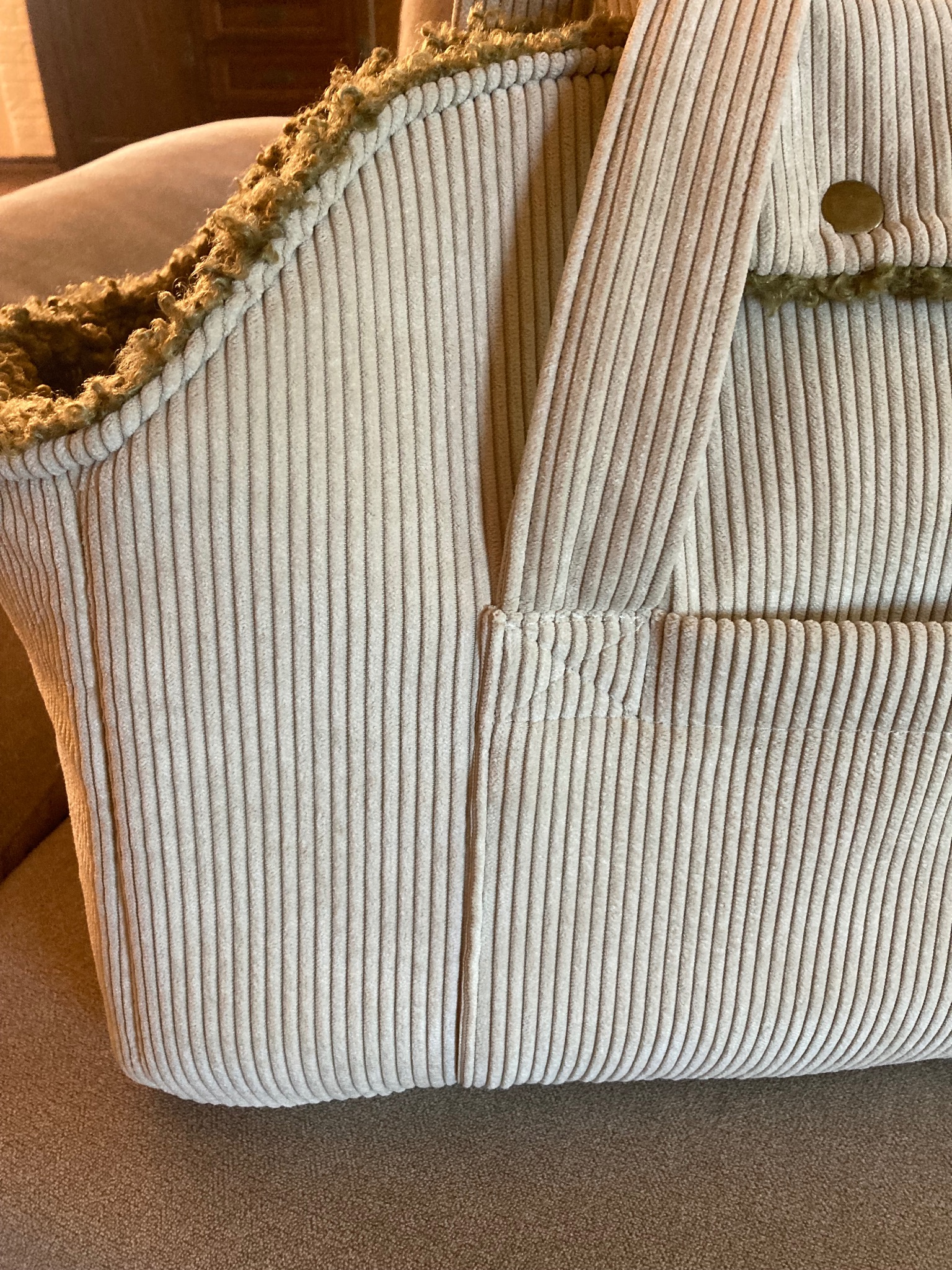 Beżowa torba z grubego sztruksu z futerkowym wykończeniem i kieszenią na zewnątrz, widoczny guzik.