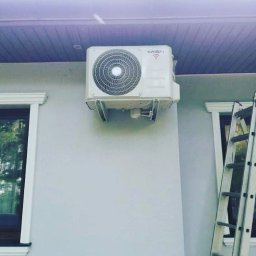 Eldar-Ice-Trans Adrian Folusiak - Biała jednostka zewnętrzna klimatyzatora marki Kaisai zamontowana na elewacji budynku, widoczna drabina oparta o ścianę.