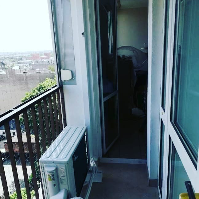 Biała jednostka zewnętrzna klimatyzacji zamontowana na balkonie z widokiem na miasto, zabezpieczona siatką przed gołębiami.