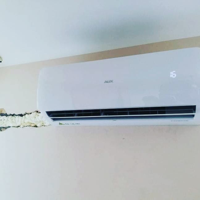 Biała jednostka klimatyzacji AUX zamontowana na ścianie, widoczne ślady pianki montażowej wokół instalacji.