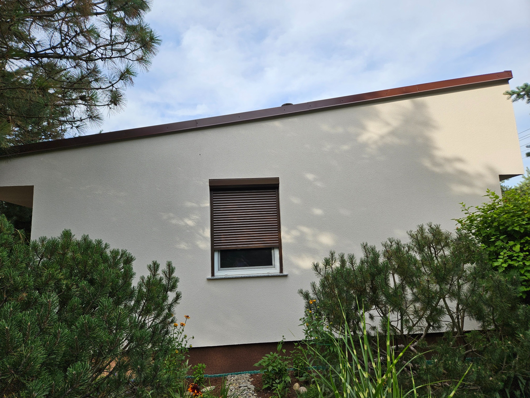 Jasna elewacja domu jednorodzinnego z brązowymi roletami w oknach, widok z poziomu ogrodu w Łubnianach.