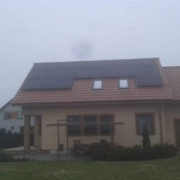 Krzysztof Szymecki - Dom jednorodzinny z panelami fotowoltaicznymi na dachu w mglisty dzień, widoczne okna dachowe i elementy wyposażenia ogrodu.