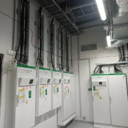 Rozdzielnice elektryczne z podłączonymi przewodami w korytach kablowych, widoczne etykiety informacyjne i lampa sufitowa