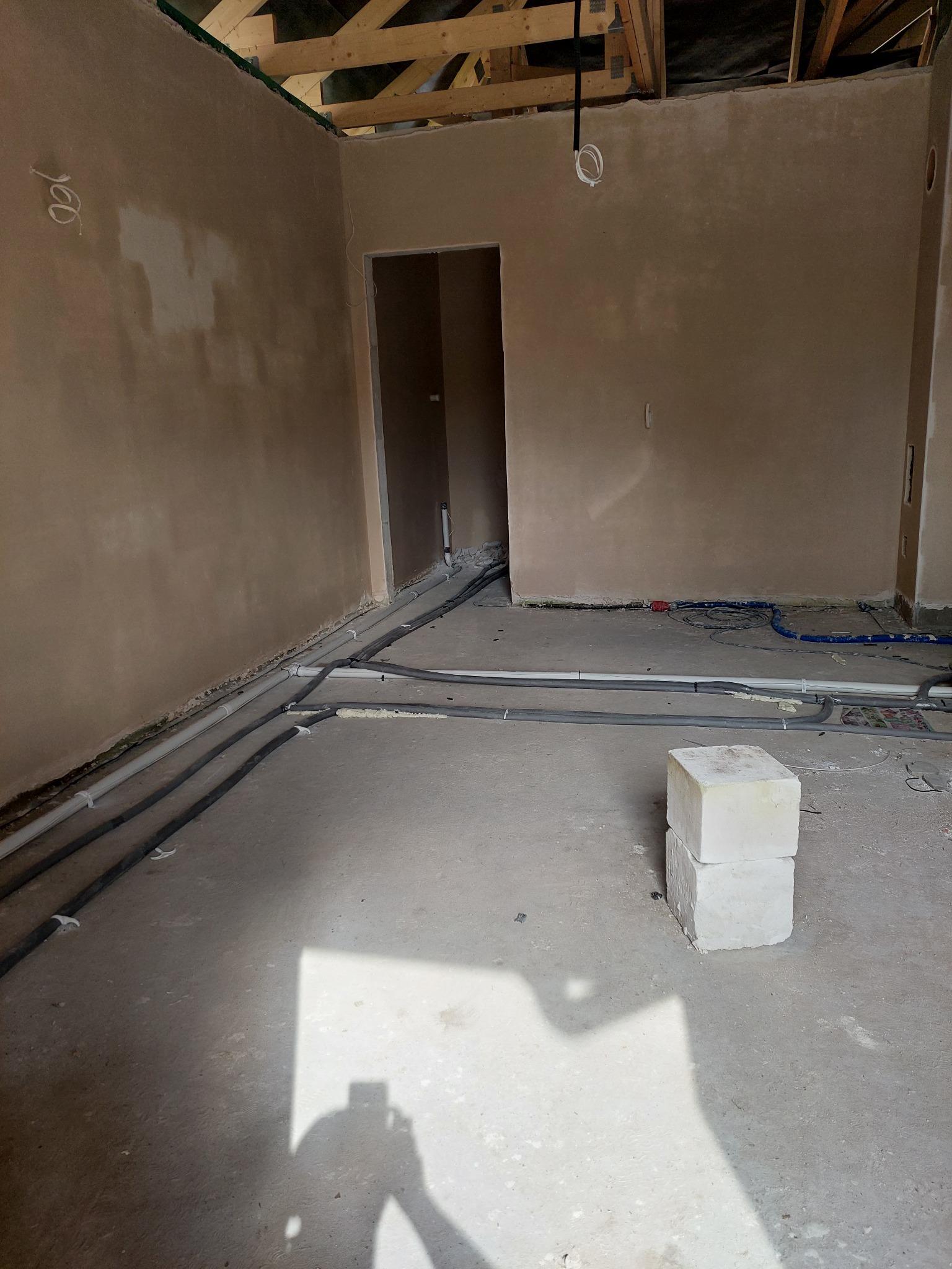 Surowy stan wnętrza z widocznymi przewodami wentylacyjnymi i elektrycznymi wzdłuż ścian, przygotowanymi do dalszych prac wykończeniowych, z dwoma bloczkami z betonu komórkowego na pierwszym planie.