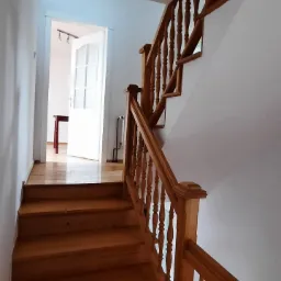 Drewniane schody z balustradą w jasnym wnętrzu, widok z dołu, parkiet na podłodze, drzwi w tle.