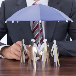 Mężczyzna w garniturze trzyma parasol nad kręgiem papierowych figurek, symbolizując ochronę grupy.