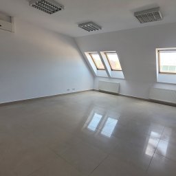 Katarzyna Kucharek, Biuro Nieruchomości REFLEX - Puste, jasne poddasze biurowe z oknami dachowymi i grzejnikami. Białe ściany, płytki na podłodze. Widoczne gniazdka elektryczne i klimatyzacja.