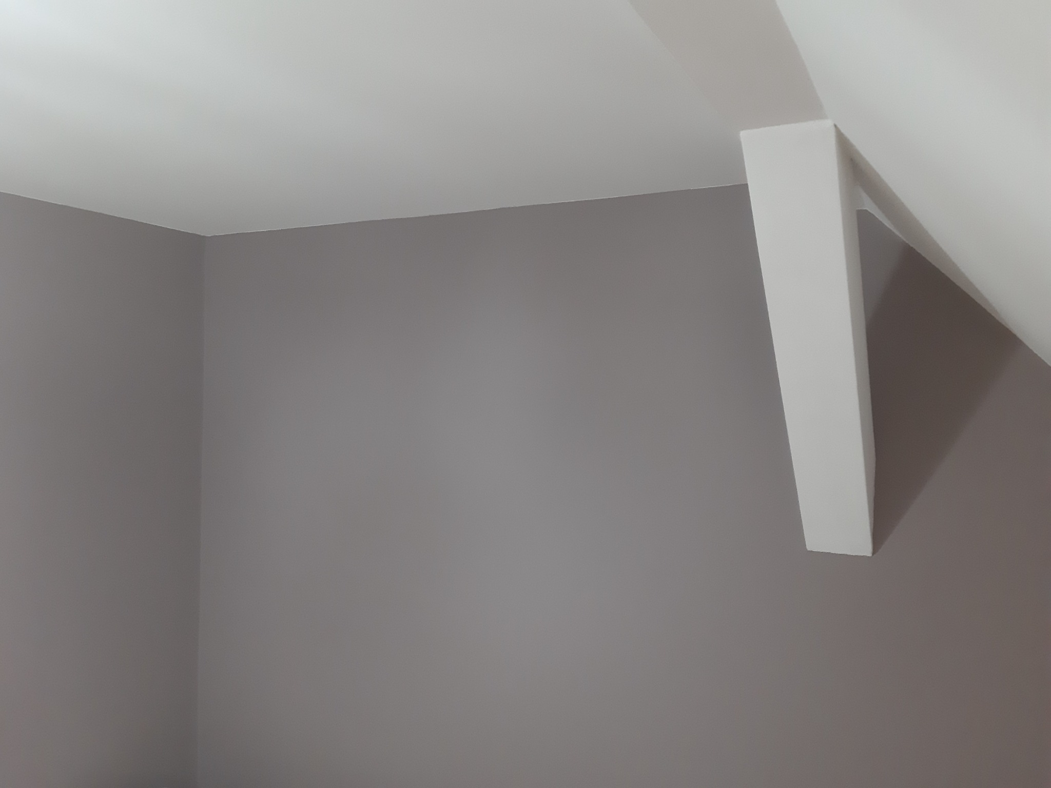 Świeżo pomalowany na szaro narożnik pokoju z białym, ukośnym słupem podtrzymującym sufit.