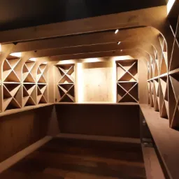 Drewniana piwniczka na wino z oświetleniem LED, z ukośnymi przegródkami na butelki, czarny sufit i drewniana podłoga.