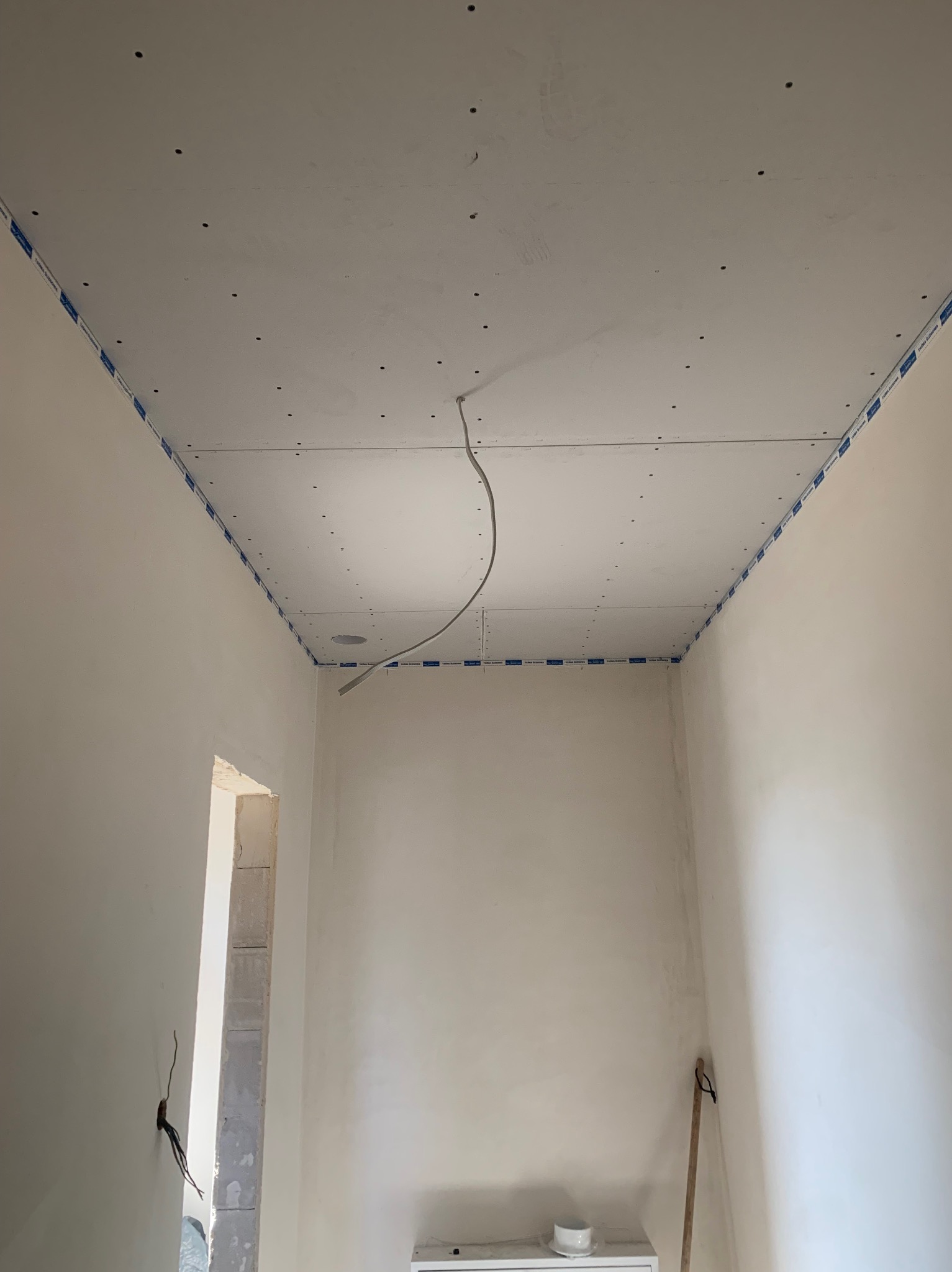 Wnętrze pokoju w trakcie montażu sufitu z płyt kartonowo-gipsowych, widoczne profile obwodowe i przewody elektryczne. Ściany przygotowane do dalszych prac wykończeniowych.