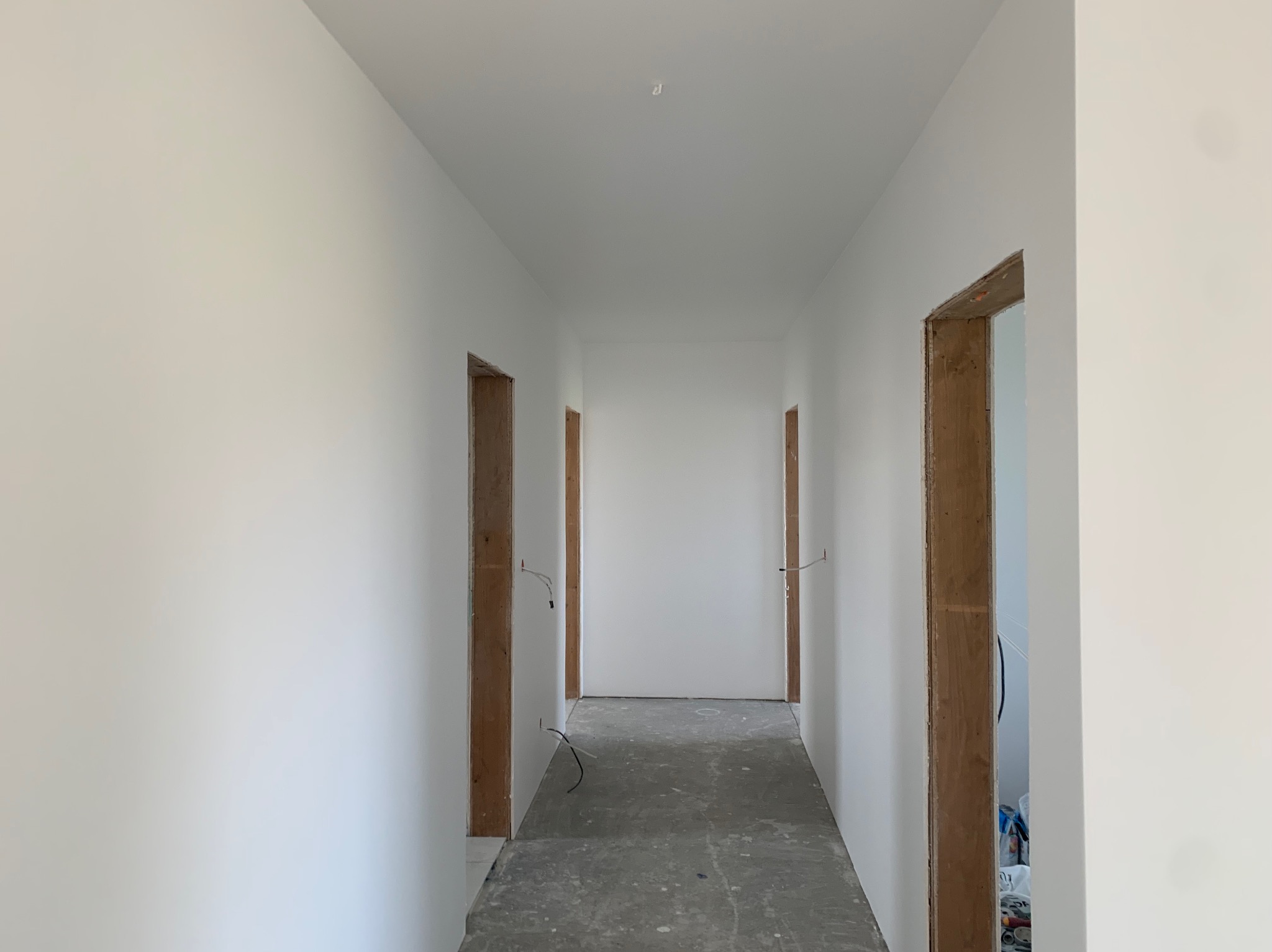 Biały korytarz po remoncie z surowymi ościeżnicami drzwi i wystającymi przewodami elektrycznymi. Świeżo pomalowane ściany i surowa podłoga.