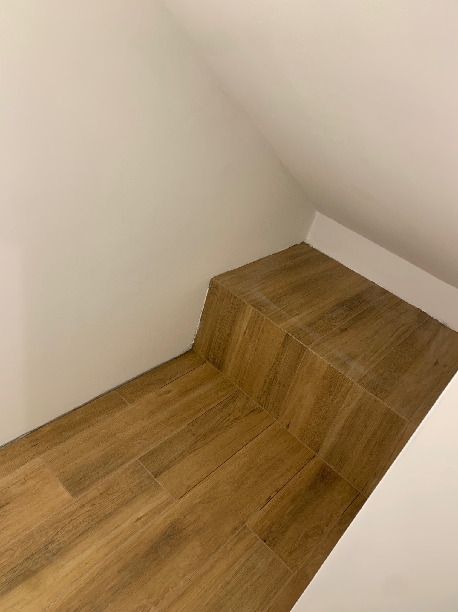 Ukończone układanie płytek imitujących drewno na podłodze w rogu pomieszczenia, widok z góry, białe ściany i sufit.