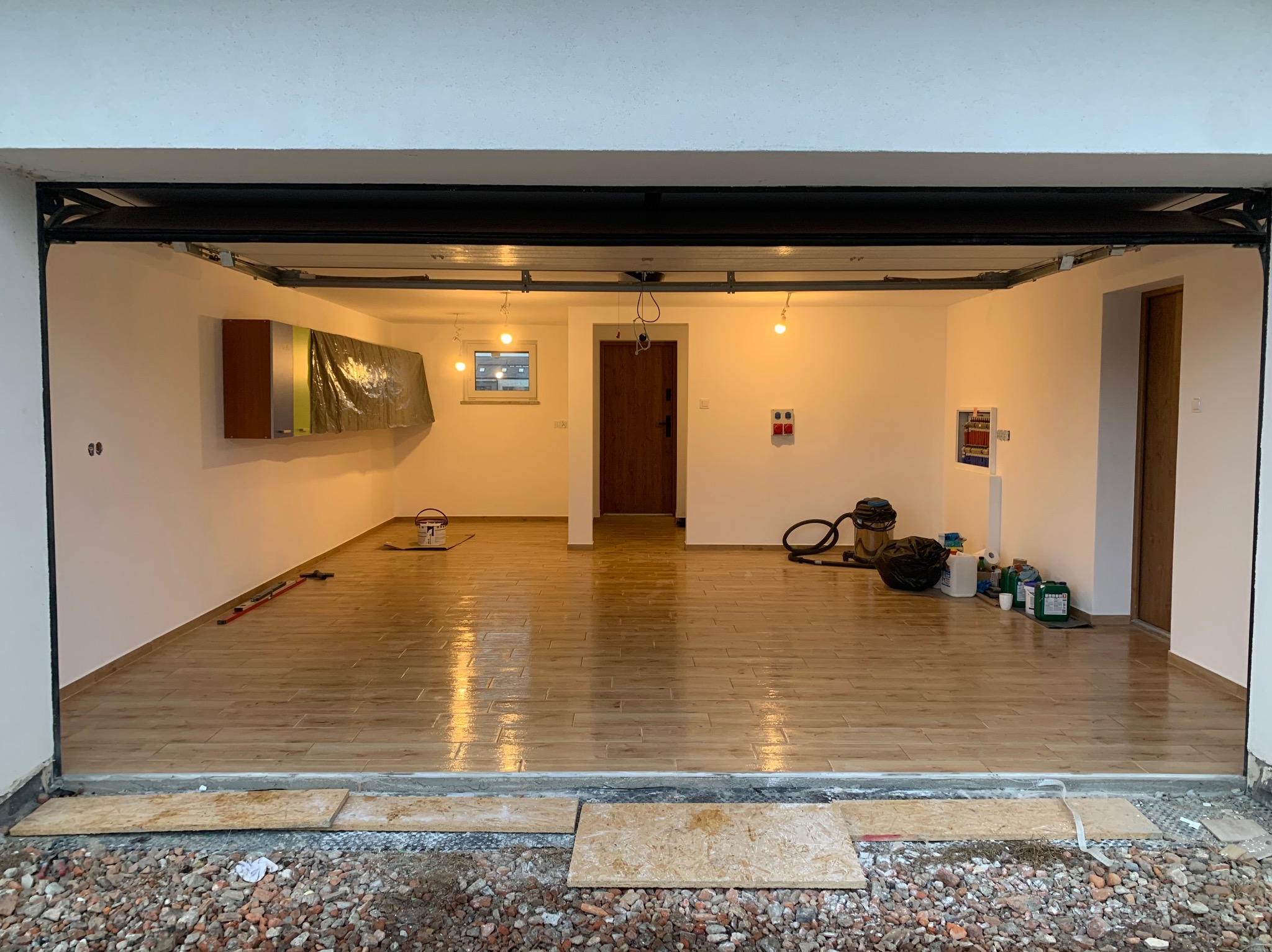 Wykończone wnętrze garażu z połyskującą, drewnopodobną podłogą z płytek, świeżo pomalowanymi ścianami i częściowo otwartą bramą garażową.