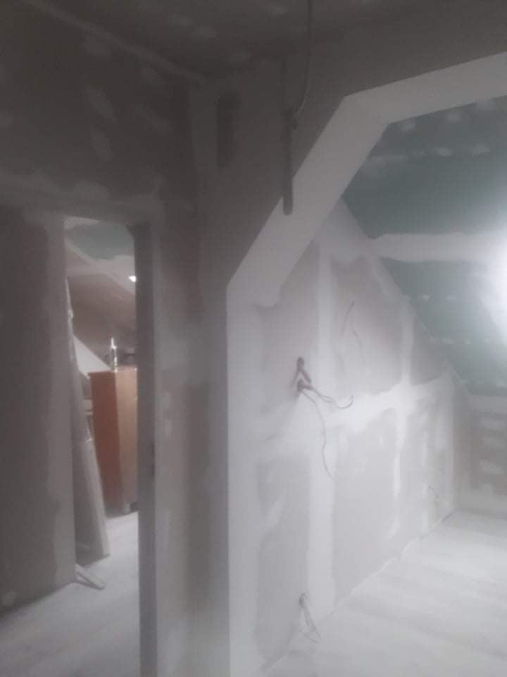 Poddasze w trakcie prac wykończeniowych: ściany z płyt kartonowo-gipsowych, widoczne kable elektryczne, surowe wykończenie, przygotowanie do dalszych prac.