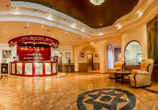 Eleganckie wnętrze salonu kosmetycznego z marmurową podłogą, recepcją z czerwonymi elementami i dwoma fotelami w stylu vintage.