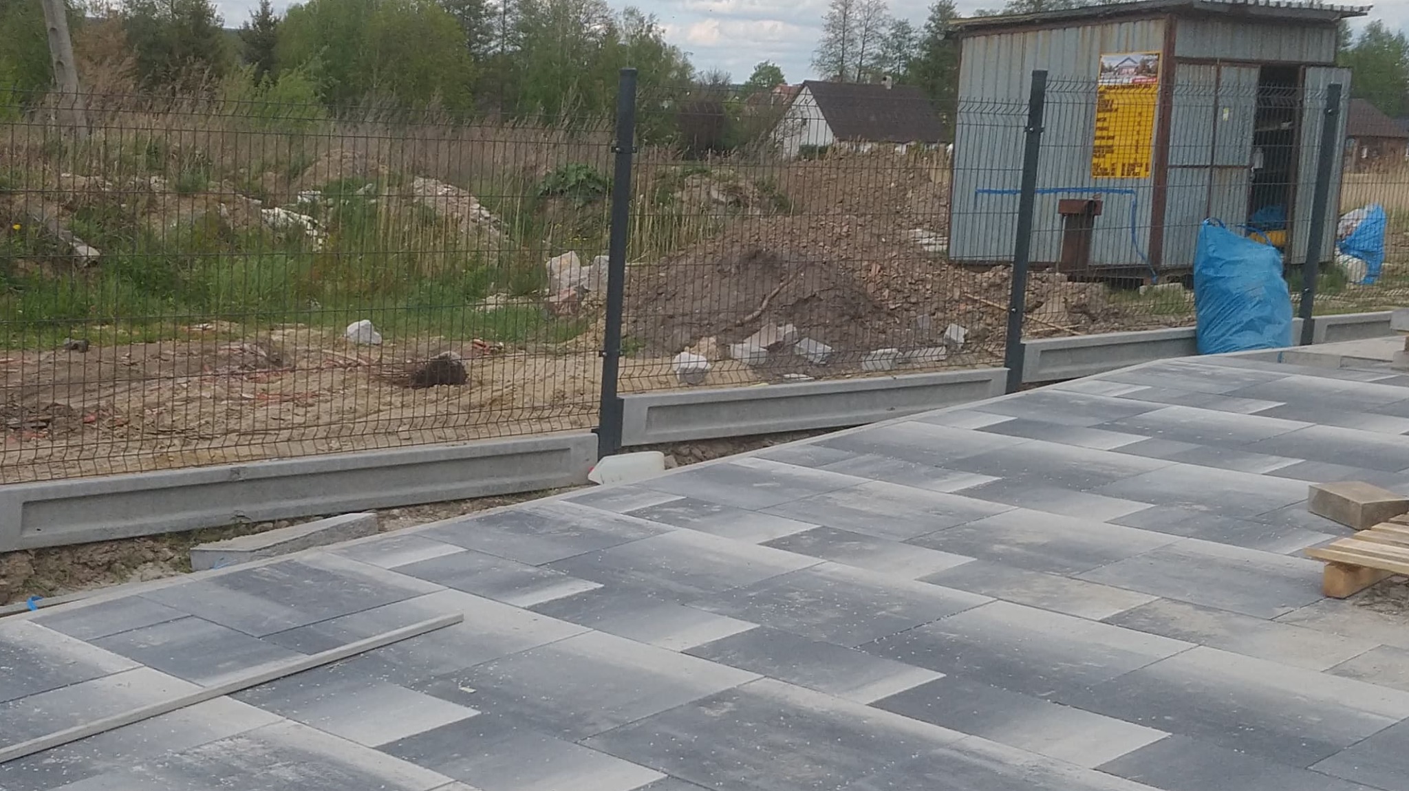 W trakcie budowy: Nowa kostka brukowa ułożona w zygzak obok fundamentów pod ogrodzenie z siatki.