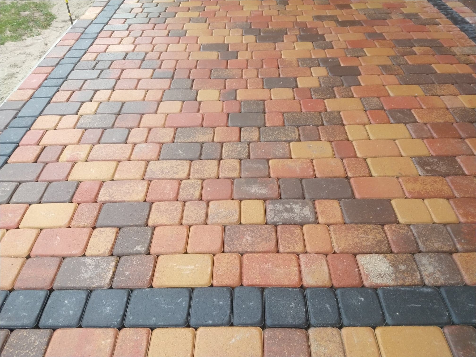 Ułożona kolorowa kostka brukowa z ciemnoszarą obwódką, widok z góry, lekki kąt.