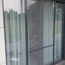 Przesuwne okno balkonowe z moskitierą w grafitowej ramie, widok z zewnątrz na taras wyłożony szarą kostką.