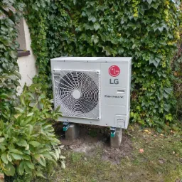 Zewnętrzna jednostka pompy ciepła LG Therma V, zamontowana na betonowych bloczkach na trawniku, z bluszczem porastającym ścianę w tle.