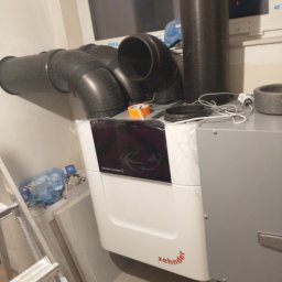 Energia Z Natury Artur Michalczyk - Rekuperator Zehnder ComfoAir Q z podłączonymi przewodami wentylacyjnymi w Kaskach, widoczna drabina i elementy instalacji.