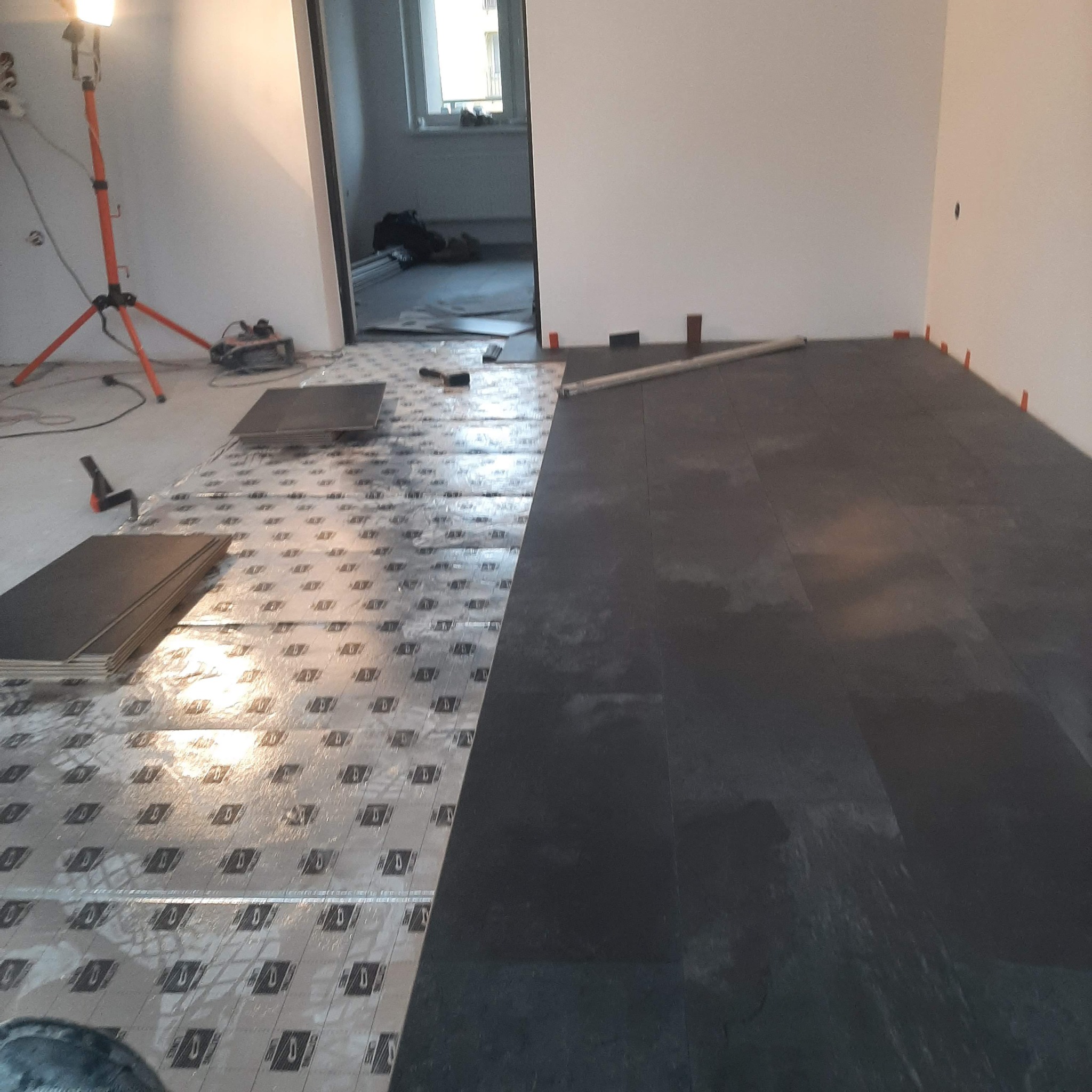 Montaż paneli podłogowych w trakcie realizacji w Tarnowskich Górach, widoczna część podkładu oraz ułożone panele, narzędzia i lampa budowlana.