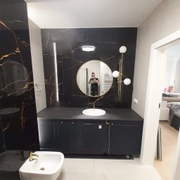 Szark-Bud - Elegancka łazienka z czarnymi płytkami imitującymi marmur, białym bidetem z pozłacaną armaturą i okrągłym lustrem z odbiciem fotografa.