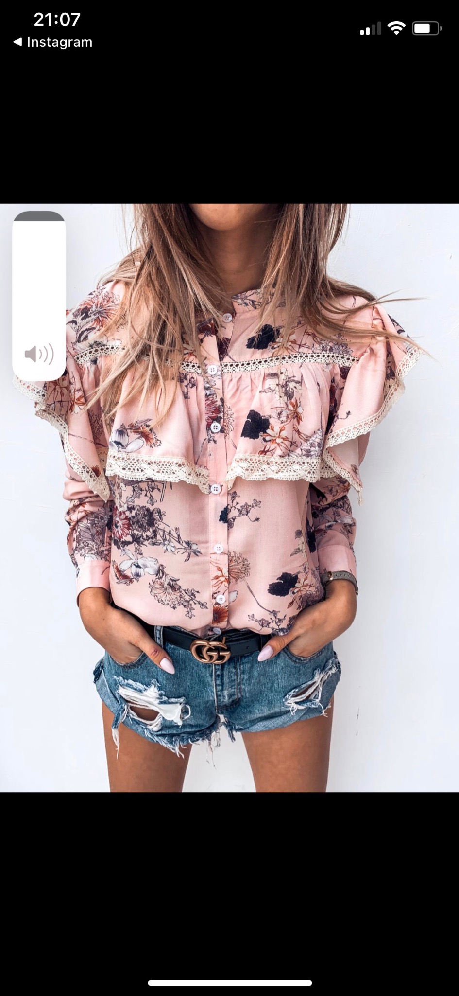 Kobieta w Lesznie prezentuje bluzkę w kwiaty z falbanami i koronką, zestawioną z krótkimi jeansowymi spodenkami i paskiem z logo.