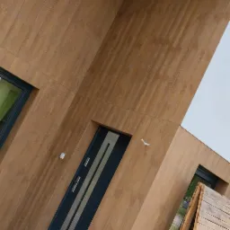 Nowoczesna elewacja budynku z panelami imitującymi drewno, antracytowe okna i drzwi, widoczny fragment drewnianej konstrukcji rusztowania.