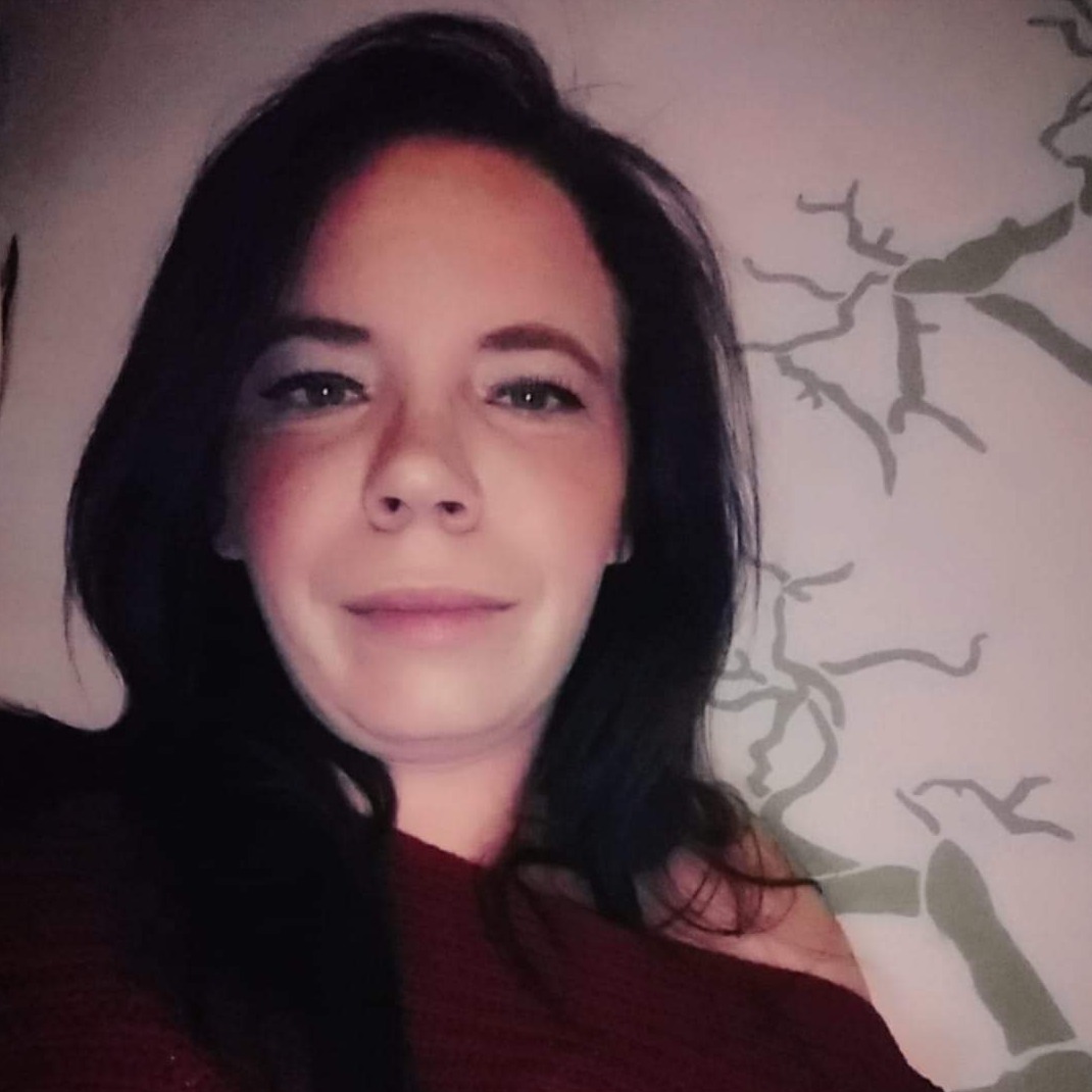 Portret uśmiechniętej kobiety o ciemnych włosach na tle wzorzystej tapety.